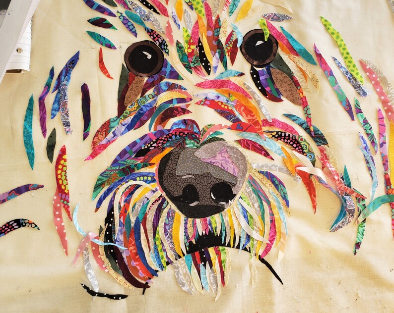 Pode incluir: Um retrato de c&atilde;o de tecido patchwork colorido com nariz e olhos pretos. O tecido &eacute; cortado em tiras longas e costurado para criar um efeito texturizado e em camadas.