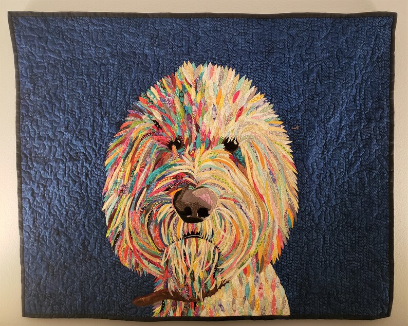 Pode incluir: Um cobertor abstrato e colorido que representa o rosto de um c&atilde;o. A pelagem do c&atilde;o &eacute; feita de v&aacute;rios tons de azul, verde, amarelo, laranja e vermelho. O nariz do c&atilde;o &eacute; marrom e seus olhos s&atilde;o pretos. O fundo do cobertor &eacute; azul escuro.