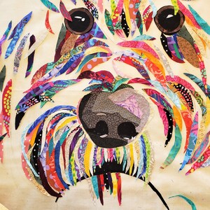 Pode incluir: Uma obra de arte de tecido patchwork colorido que representa o rosto de um c&atilde;o. A pelagem do c&atilde;o &eacute; feita de v&aacute;rios peda&ccedil;os de tecido coloridos, e os olhos e o nariz s&atilde;o pretos.