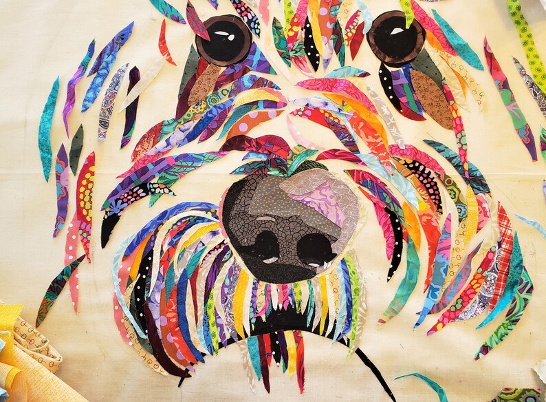 Pode incluir: Uma obra de arte de tecido patchwork colorido que representa o rosto de um c&atilde;o. A pelagem do c&atilde;o &eacute; feita de v&aacute;rios peda&ccedil;os de tecido coloridos, e os olhos e o nariz s&atilde;o pretos.