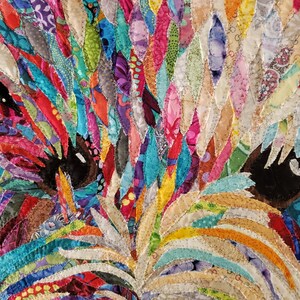 Pode incluir: Um close-up de uma obra de arte de tecido colorida que retrata o rosto de um c&atilde;o. A pelagem do c&atilde;o &eacute; feita de muitos peda&ccedil;os de tecido de diferentes cores, criando uma apar&ecirc;ncia texturizada e abstrata. Os olhos do c&atilde;o s&atilde;o pretos e castanhos, e os peda&ccedil;os de tecido s&atilde;o dispostos de forma a criar uma sensa&ccedil;&atilde;o de profundidade e dimens&atilde;o.