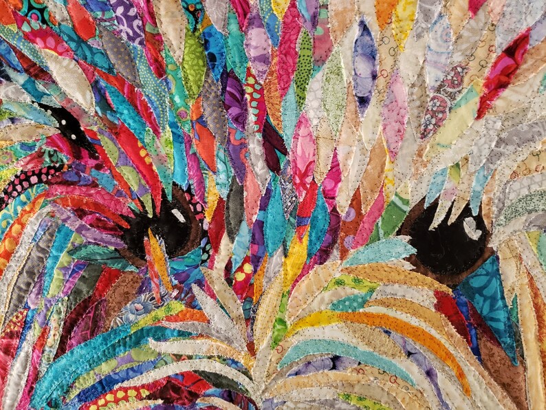 Pode incluir: Um close-up de uma obra de arte de tecido colorida que retrata o rosto de um c&atilde;o. A pelagem do c&atilde;o &eacute; feita de muitos peda&ccedil;os de tecido de diferentes cores, criando uma apar&ecirc;ncia texturizada e abstrata. Os olhos do c&atilde;o s&atilde;o pretos e castanhos, e os peda&ccedil;os de tecido s&atilde;o dispostos de forma a criar uma sensa&ccedil;&atilde;o de profundidade e dimens&atilde;o.