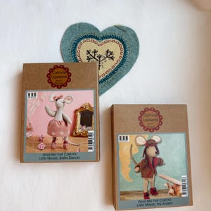 Op de afbeelding: Twee knutselpakketten met vilten muizen, een balletdanseres en de andere een piloot, met de tekst "Corinne Lapierre" op de dozen. Een blauwe hartvormige vilten decoratie met geborduurde details is ook zichtbaar.
