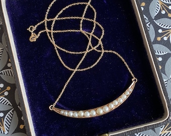 Op de afbeelding: Een gouden ketting met een halve maan hanger bezet met witte parels. De ketting wordt gepresenteerd in een blauwe fluwelen doos.