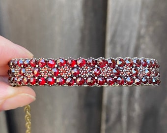 May include: A silver bracelet with a double row of red garnet stones. The bracelet is made of small, round stones set in a silver band.