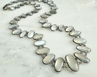 May include: A silver chain necklace with oval-shaped moonstone beads. The necklace is approximately 20 inches long and features a delicate chain design.