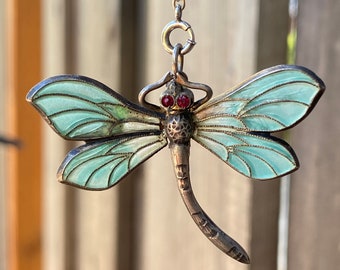 May include: A silver dragonfly pendant with blue enamel wings and red gemstone eyes. The pendant is on a silver chain.