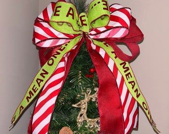 May include: A red and white striped ribbon bow with the words "A Mean One" and "E.A.E." in green on a small Christmas tree with red berries and a gold reindeer ornament.