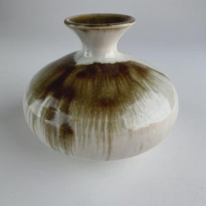 Op de afbeelding: Een keramische vaas met een ronde body en een smalle hals. De vaas is voornamelijk wit met een bruin, gedruppeld glazuureffect dat het bovenste deel van de body bedekt. De rand van de vaas is donkerbruin.