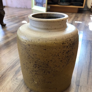 May include: A large, ceramic vase with a speckled, brown and white glaze. The vase has a rounded body and a wide opening.
