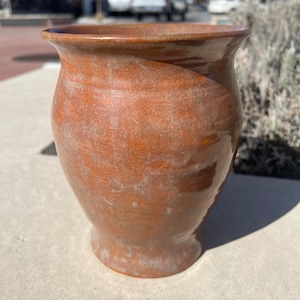 Op de afbeelding: Een bruine keramische vaas met een gespikkeld glazuur. De vaas heeft een ronde bodem en een uitlopende opening.