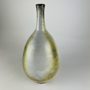 May include: A ceramic vase with a narrow neck and a rounded, bulbous body. The surface features a gradient of muted white and grey tones transitioning into a textured, mottled olive green and dark brown finish, with a dark brown rim at the top.