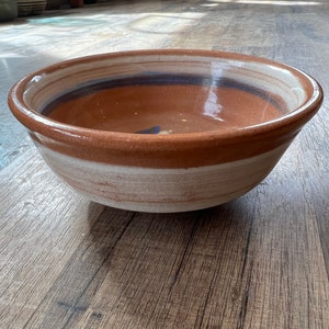 Peut inclure: Un grand bol en céramique brun avec un glaçage blanc et bleu. Le bol a un bord large et arrondi et une finition lisse et brillante.