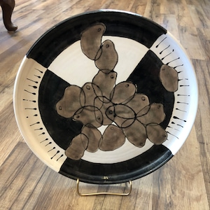 Può includere: Un piatto in ceramica bianco e nero con un design di forme astratte grigie. Il piatto ha un bordo bianco e nero con punti bianchi.