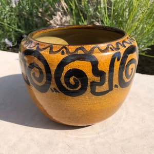 May include: A brown ceramic planter with black swirl designs. The planter has a rounded shape and a slightly flared rim.