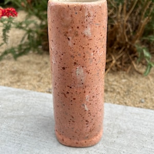 May include: A speckled, light pink ceramic vase with a white rim. The vase has a cylindrical shape and a textured surface.