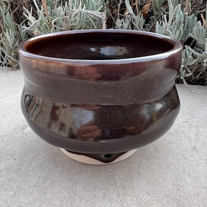 May include: A dark brown ceramic bowl with a white base. The bowl has a rounded shape and a slightly flared rim.