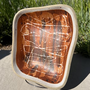 May include: A white ceramic rectangular dish with a brown and white glaze. The glaze has a streaky pattern with white lines on a brown background.