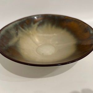 Könnte beinhalten: Eine kleine, flache Keramikschale mit brauner, weißer und grüner Glasur. Die Schale hat einen leicht abgerundeten Boden und einen breiten, flachen Rand.