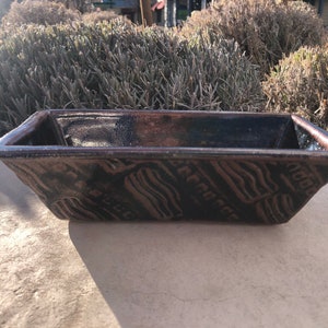 May include: A rectangular ceramic dish with a dark brown glaze and a wavy pattern. The dish has a slightly raised rim and is made of stoneware.