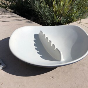 May include: White ceramic ashtray with a blue rim and a built-in cigarette rest. The ashtray is shaped like a shallow bowl with a raised, curved section in the centre.