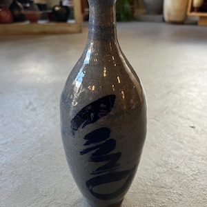 Può includere: Un vaso alto in ceramica grigia con bordo e base blu scuro. Il vaso presenta pennellate blu scuro sul davanti. Il vaso ha una finitura liscia e lucida ed è probabilmente fatto a mano. Questo vaso decorativo è adatto per l'arredamento della casa.