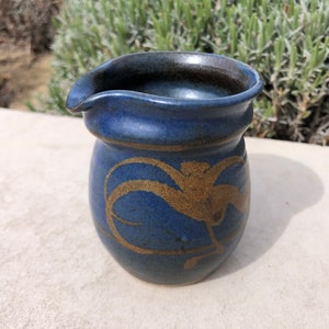 May include: A small blue ceramic pitcher with a brown rim and gold painted design.