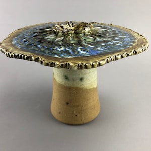 May include: A ceramic mushroom sculpture with a blue and brown glazed top and a tan base.
