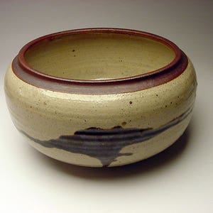 May include: A ceramic bowl with a brown rim and a white glaze. The bowl has a dark brown glaze design on the bottom.