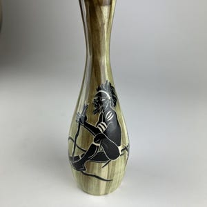 May include: A decorative vase with a slender neck and a wide base. The vase has a green and brown striped pattern. A black silhouette of a person with a staff is painted on the front of the vase.