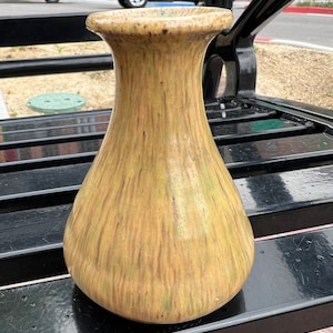 Puede incluir: Un jarrón de cerámica amarillo y marrón con una superficie texturizada. El jarrón tiene una base ancha y un cuello estrecho.