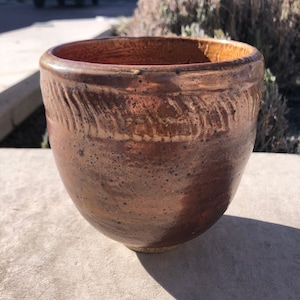 May include: A brown ceramic planter with a textured surface and a slightly flared rim. The planter has a speckled brown glaze with a hint of gold.
