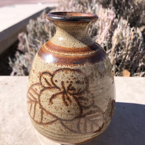 May include: A small, brown and tan ceramic vase with a floral design. The vase has a rounded body and a narrow neck.