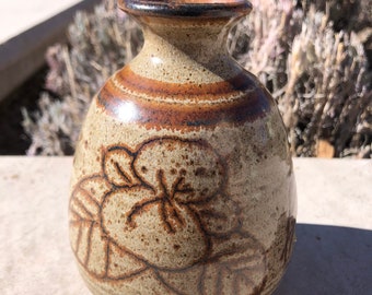 May include: A small, brown and tan ceramic vase with a floral design. The vase has a rounded body and a narrow neck.