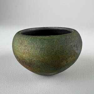 May include: A handcrafted, textured ceramic bowl with a rounded shape. The exterior features a blend of green, gold, and brown hues, creating a unique, earthy aesthetic. The interior is dark, contrasting with the exterior. This decorative bowl is suitable for home decor.