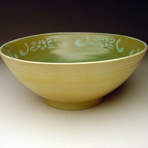 May include: A large, yellow ceramic bowl with a green glaze and a floral design around the rim.