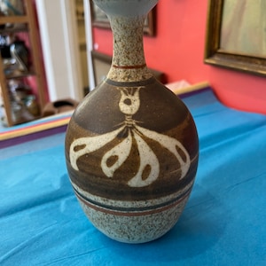 May include: A brown and white ceramic vase with a geometric design. The vase has a narrow neck and a rounded body.