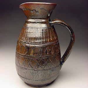 May include: A brown ceramic pitcher with a wide mouth and a handle. The pitcher has a textured surface with a geometric pattern.