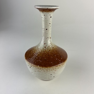 May include: A ceramic vase with a bulbous base and a slender neck. The vase is primarily white with speckled detailing and a band of brown near the base. The rim is a light gray color. A decorative piece for the home.