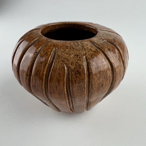 May include: A brown ceramic vase with a textured, ribbed exterior. The vase has a wide, open top and a rounded shape. The color is a mix of light and dark browns, giving it a natural, earthy appearance. The vase is likely for decorative purposes.