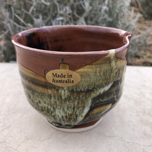 May include: A brown and green ceramic bowl with a white rim and a gold label that says "Made in Australia".