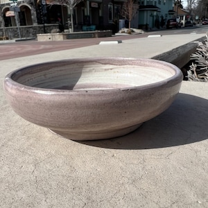 May include: A large, light purple ceramic bowl with a white glaze. The bowl has a slightly rounded bottom and a wide, shallow opening.