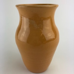 May include: A ceramic vase with a rounded body and a wide mouth. The vase is a deep yellow color with a glossy finish.