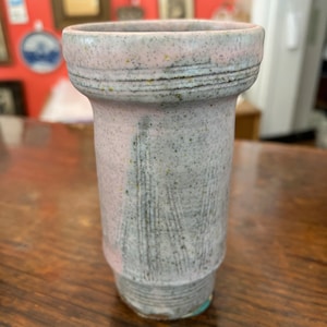 Può includere: Un piccolo vaso in ceramica rosa e grigio con una superficie testurizzata. Il vaso ha un'ampia apertura e una base stretta.