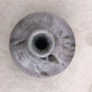 Könnte beinhalten: Eine weiße Keramikvase mit gesprenkeltem Überzug und einer breiten Öffnung. Die Vase hat eine abgerundete Form und eine strukturierte Oberfläche.