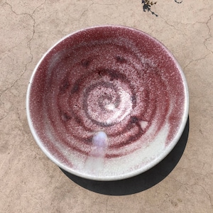 Peut inclure: Un bol en céramique blanche avec un motif en spirale rouge et blanc. Le bol est légèrement moucheté et a une finition brillante.