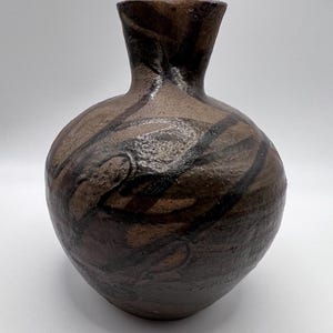 Puede incluir: Un jarrón de cerámica hecho a mano con un cuerpo redondeado y un cuello estrecho. El jarrón presenta un patrón de remolino marrón y negro. El jarrón mide aproximadamente 20 cm de alto.