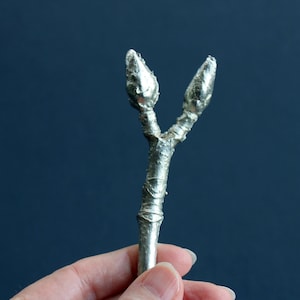 May include: A silver metal twig with two buds at the top. The twig is textured and has a smooth, polished finish.