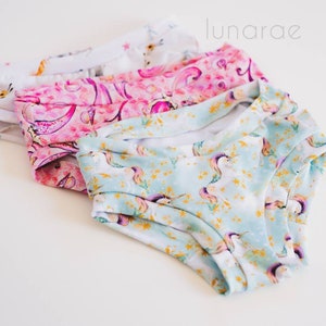 May include: Three pairs of colorful underwear with a unicorn print. The underwear is made of soft, stretchy fabric and features a variety of colors, including pink, blue, and white.