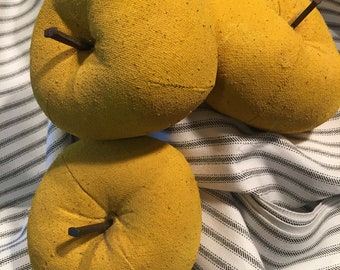 May include: Four yellow fabric apples with brown stems on a white and black striped surface.